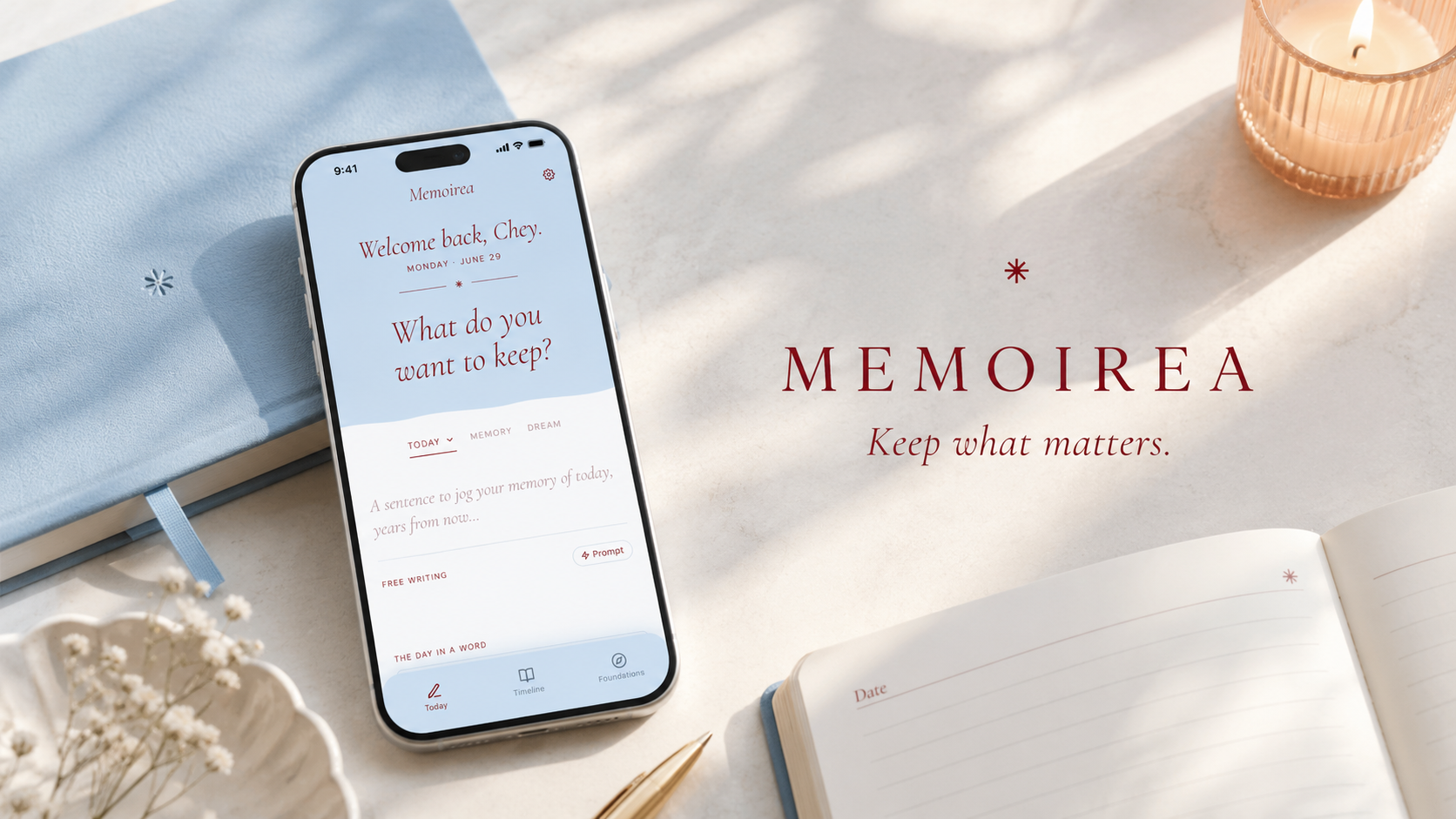 A phone showing the Memoirea writing prompt What do you want to keep, resting on a pale blue journal beside a lit candle, dried flowers and an open notebook