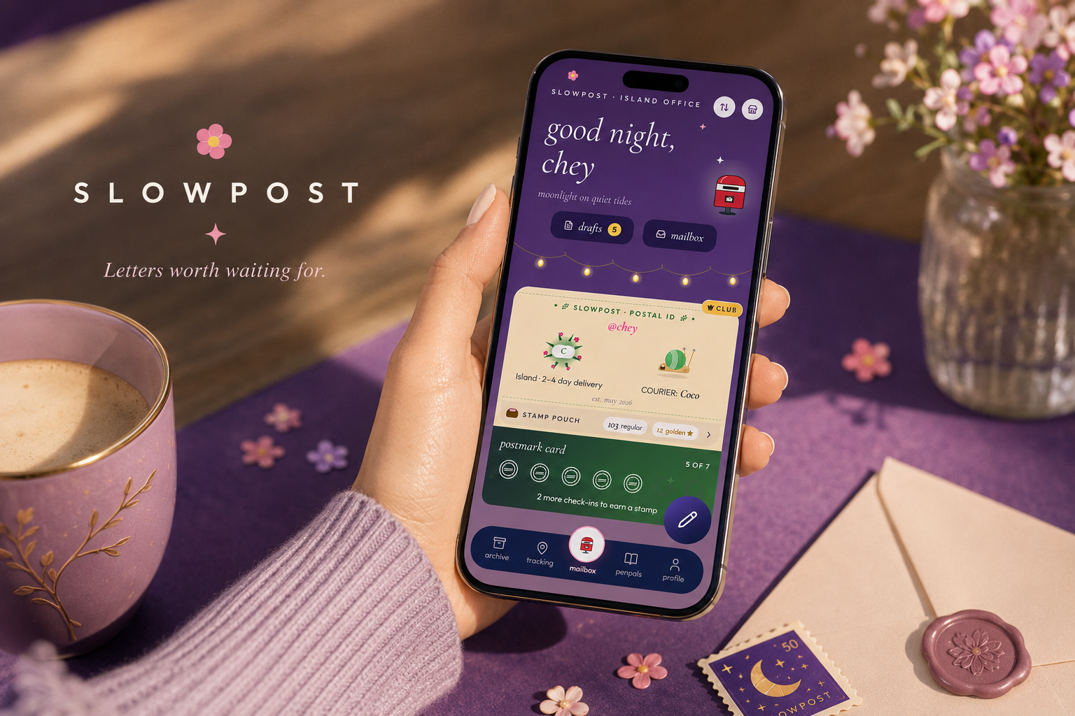 A hand in a lavender sweater holding a phone showing the Slowpost mailbox and postal ID card, beside a latte, scattered blossoms and a cream envelope sealed with wax